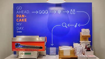 A breakfast station with a flat-top griddle for pancakes, a coffee machine, and a sign directing to the breakfast area.