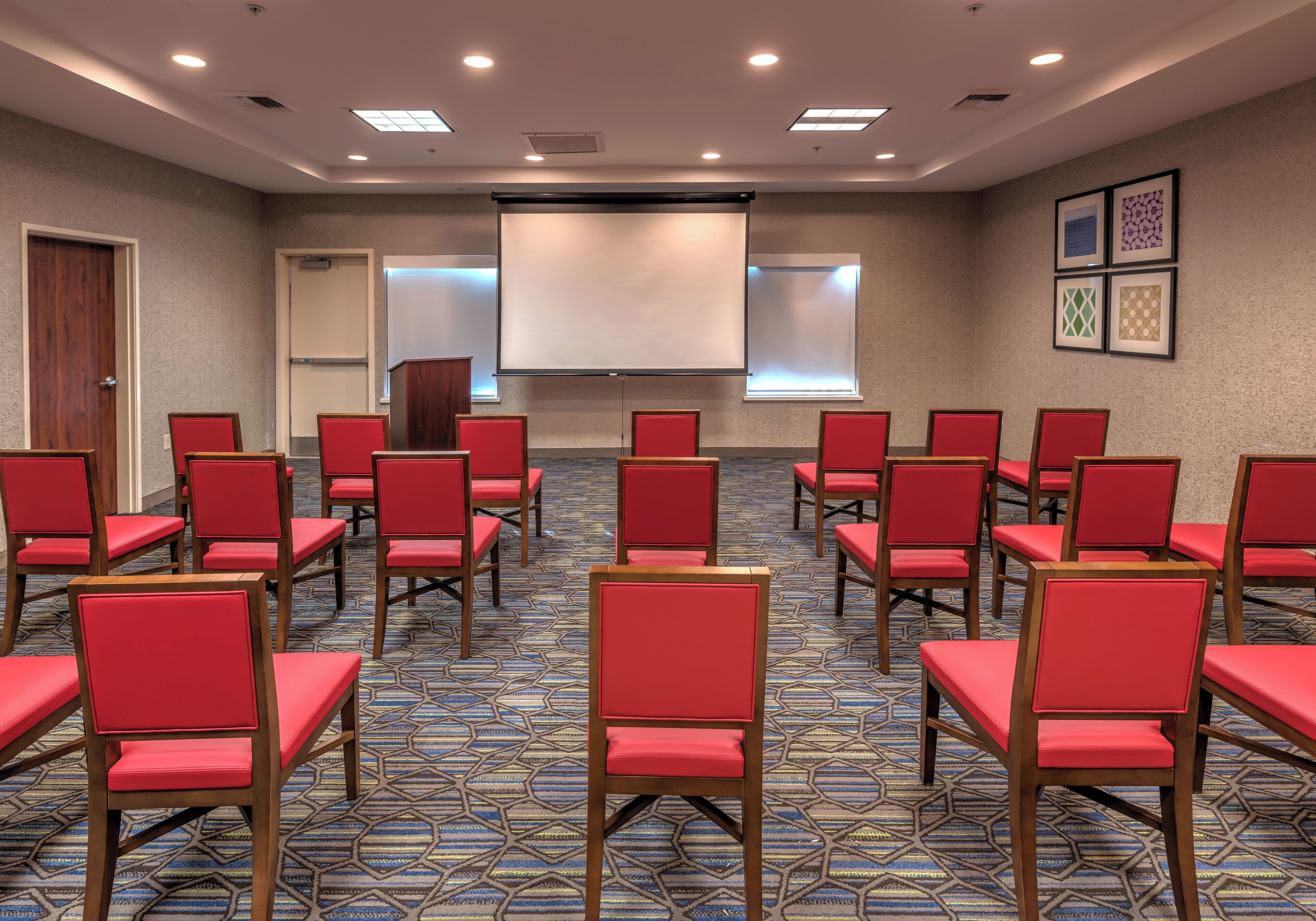 Una sala conferenze con file di sedie rosse, uno schermo per proiettore e una moquette fantasia.