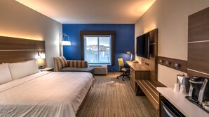 A hotel room with a large bed, a desk with a coffee maker, a TV, and a view of a body of water through a window. - Holiday Inn Express Hotel & Suites Minden by IHG (Minden)
