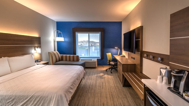 A hotel room with a large bed, a desk with a coffee maker, a TV, and a view of a body of water through a window. - Holiday Inn Express Hotel & Suites Minden by IHG (Minden)