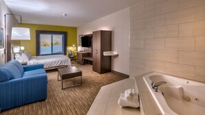 A modern hotel room with a bed, a blue sofa, a desk with a chair, a large window, and a bathtub. - Holiday Inn Express Hotel & Suites Minden by IHG (Minden)