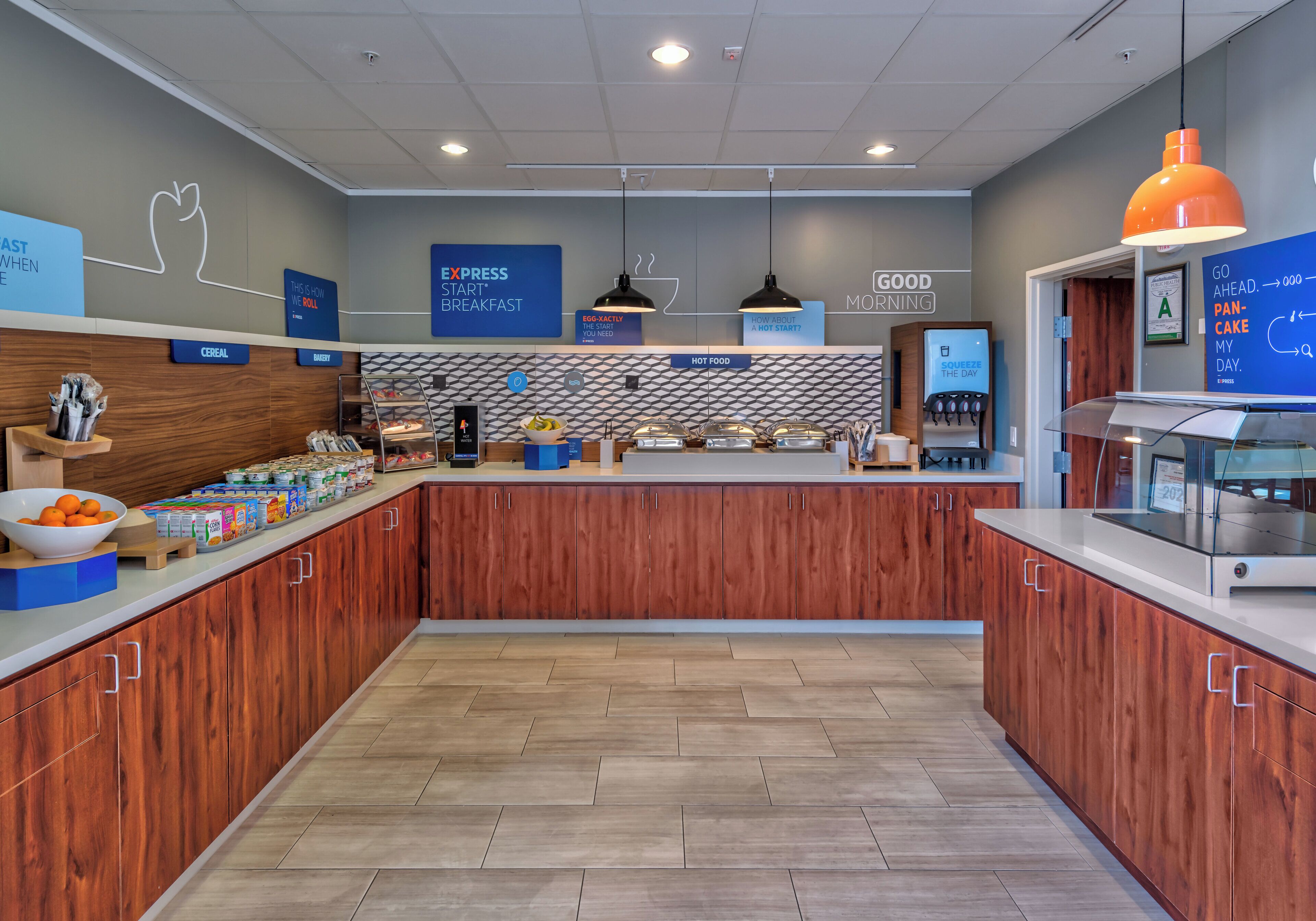 Um espaço de café da manhã moderno com um balcão central, diversas estações de comida e placas informativas.