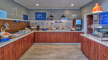 Um espaço de café da manhã moderno com um balcão central, diversas estações de comida e placas informativas.