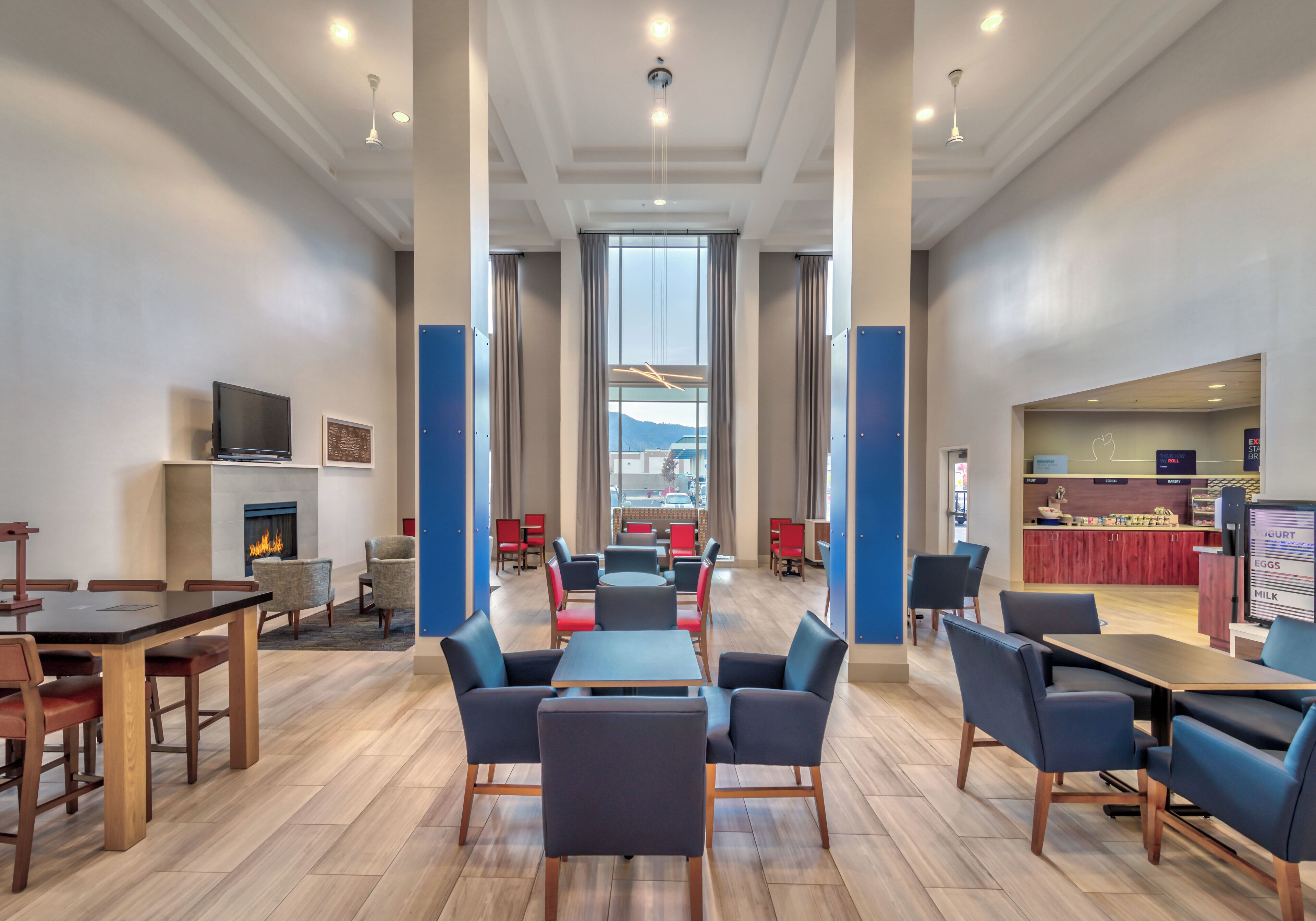 A modern hotel lobby with a central seating area, a fireplace, and a breakfast bar.