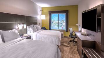 A hotel room with two beds, a desk, a TV, and a window with a view of the outside.