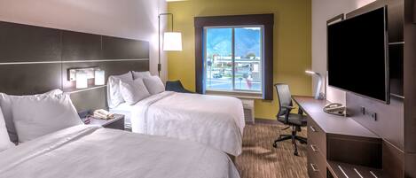 A hotel room with two beds, a desk, a TV, and a window with a view of the outside.