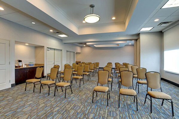 A conference room with rows of chairs, a kitchenette, and a large window.