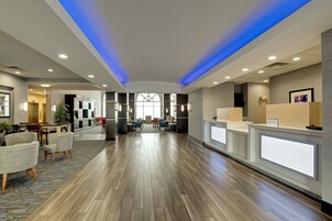 Un vestíbulo amplio con suelo de madera, mostrador de recepción, zona de estar y un gran ventanal.