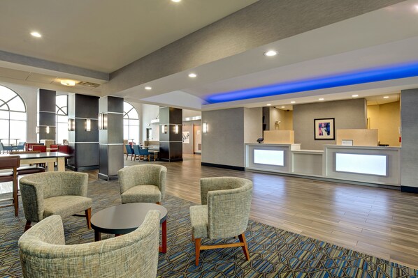 A modern hotel lobby with seating areas, a reception desk, and a view of the dining area.