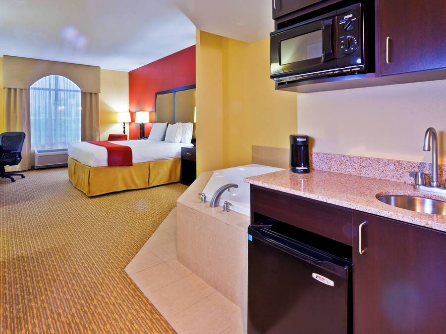 A hotel room with a bed, a desk, a microwave, a sink, and a view of the outdoors.