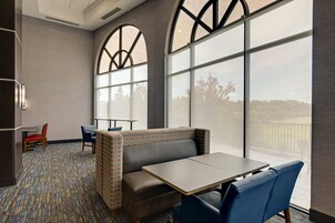 Una habitación de hotel moderna con un ventanal grande, una zona de estar con una mesa y una alfombra estampada.