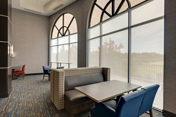 Una habitación de hotel moderna con un ventanal grande, una zona de estar con una mesa y una alfombra estampada.