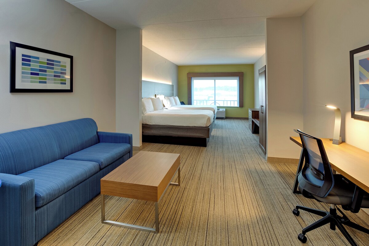 Habitación de hotel con sofá azul, una mesa de madera, cama con colchón, escritorio con silla y un ventanal grande.
