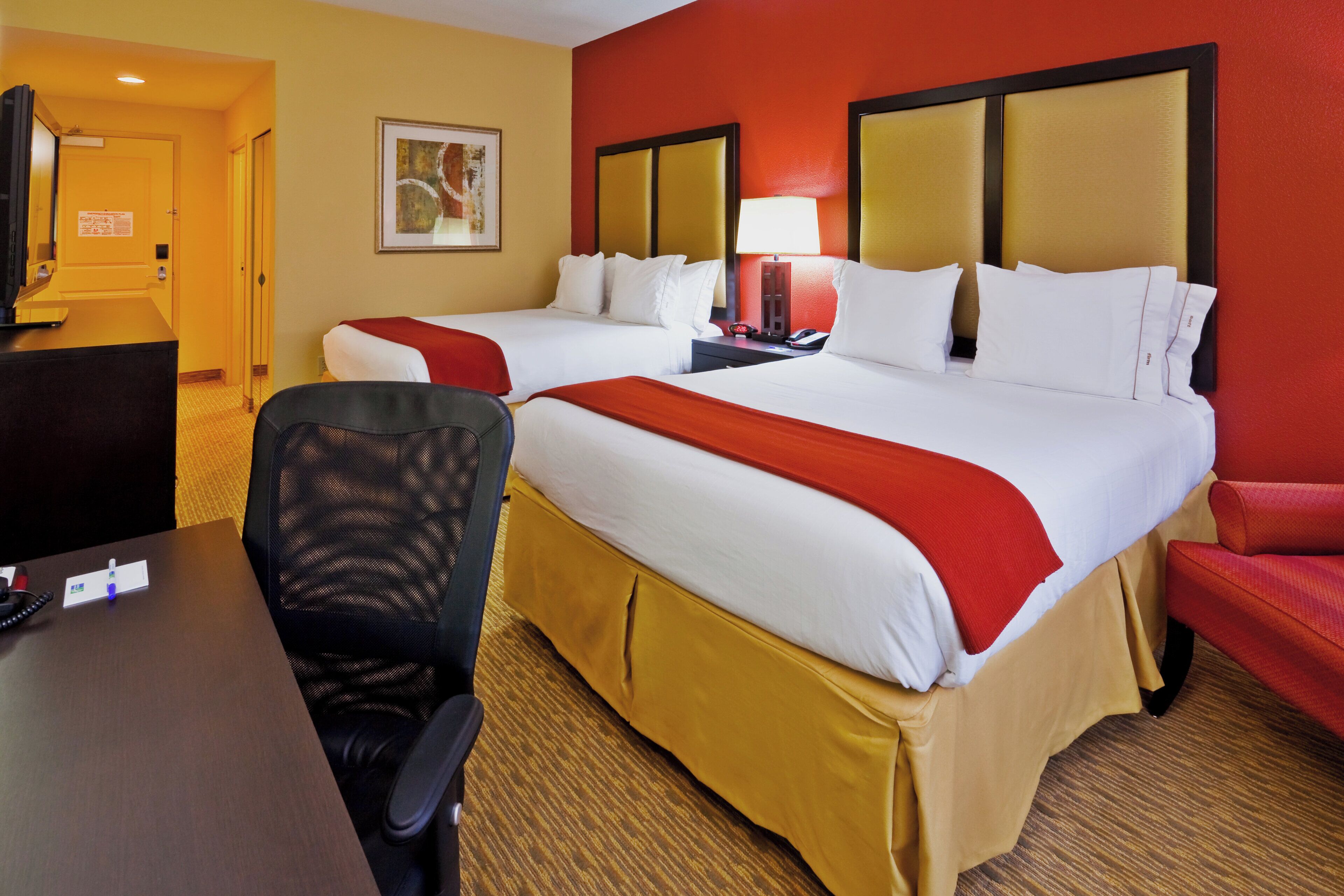 A hotel room with two beds, a desk, a chair, and a television.