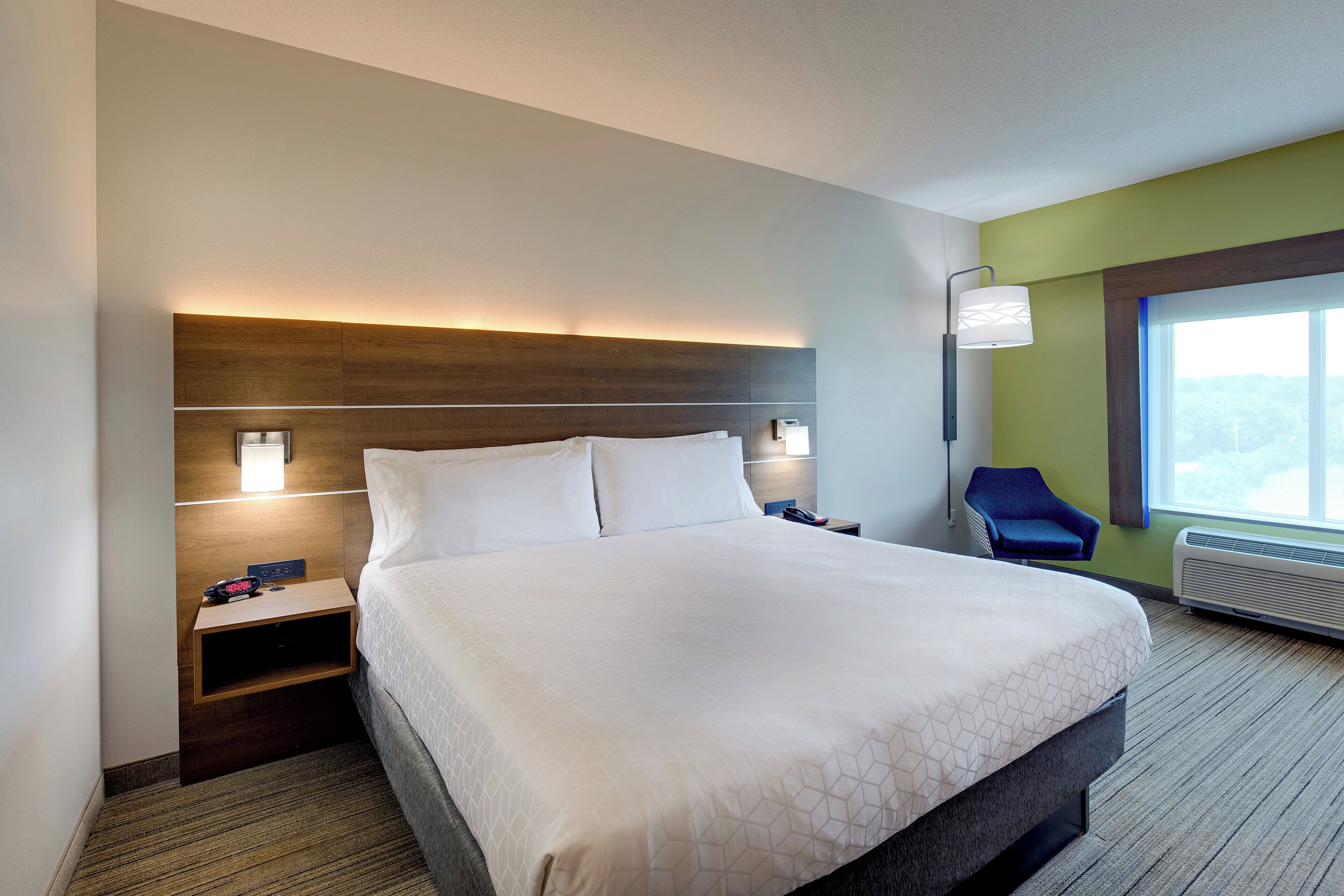 A hotel room with a large bed, bedside tables, a chair, and a window with a view.
