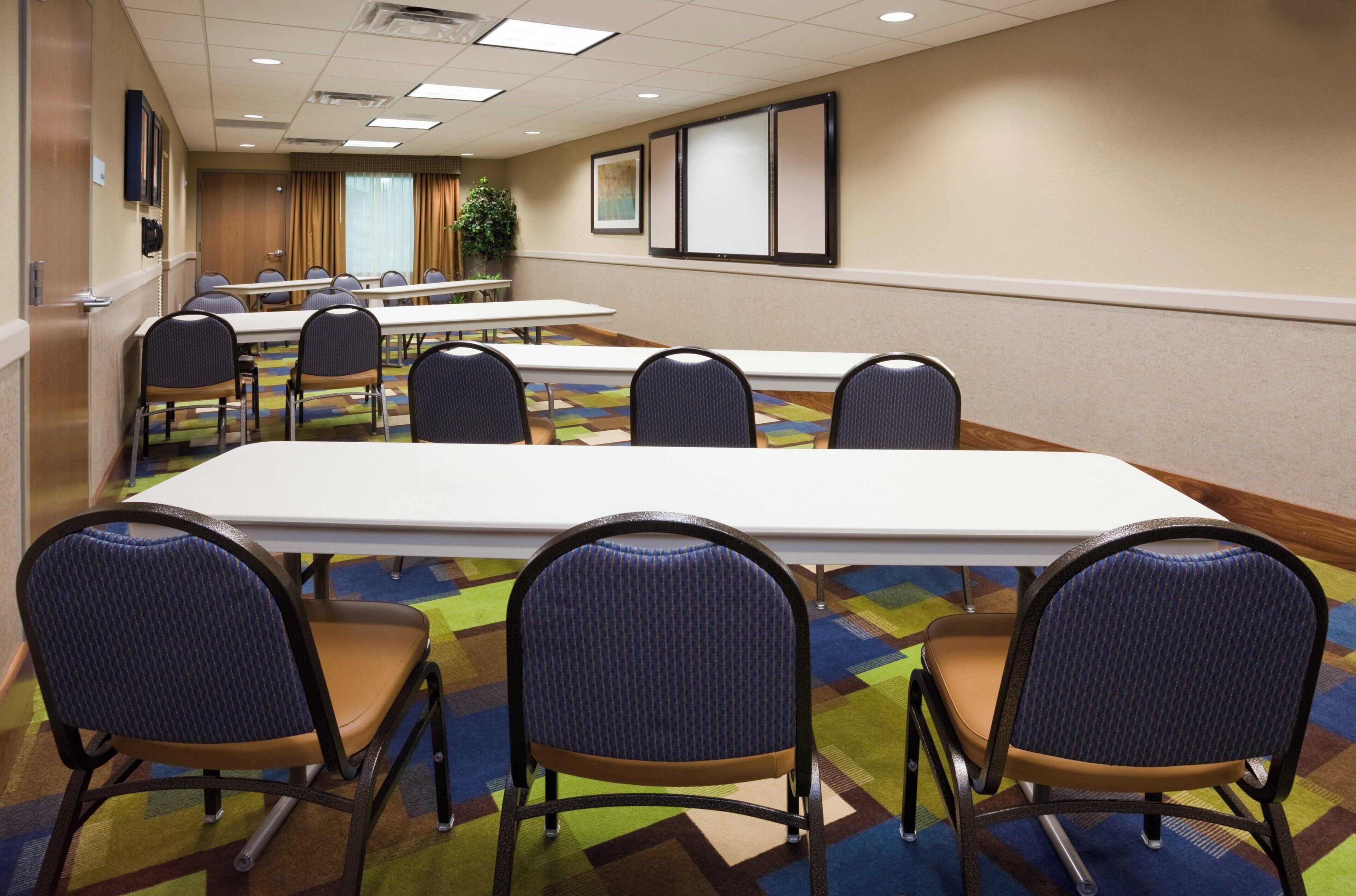 A conference room with a long table and six chairs, carpeted floor, and a plant in the background.