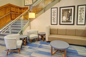 A hotel lobby with a staircase, a sofa, two armchairs, a small table, and three framed artworks on the wall. - Holiday Inn Express Hotel and Suites Mankato East by IHG (Mankato)