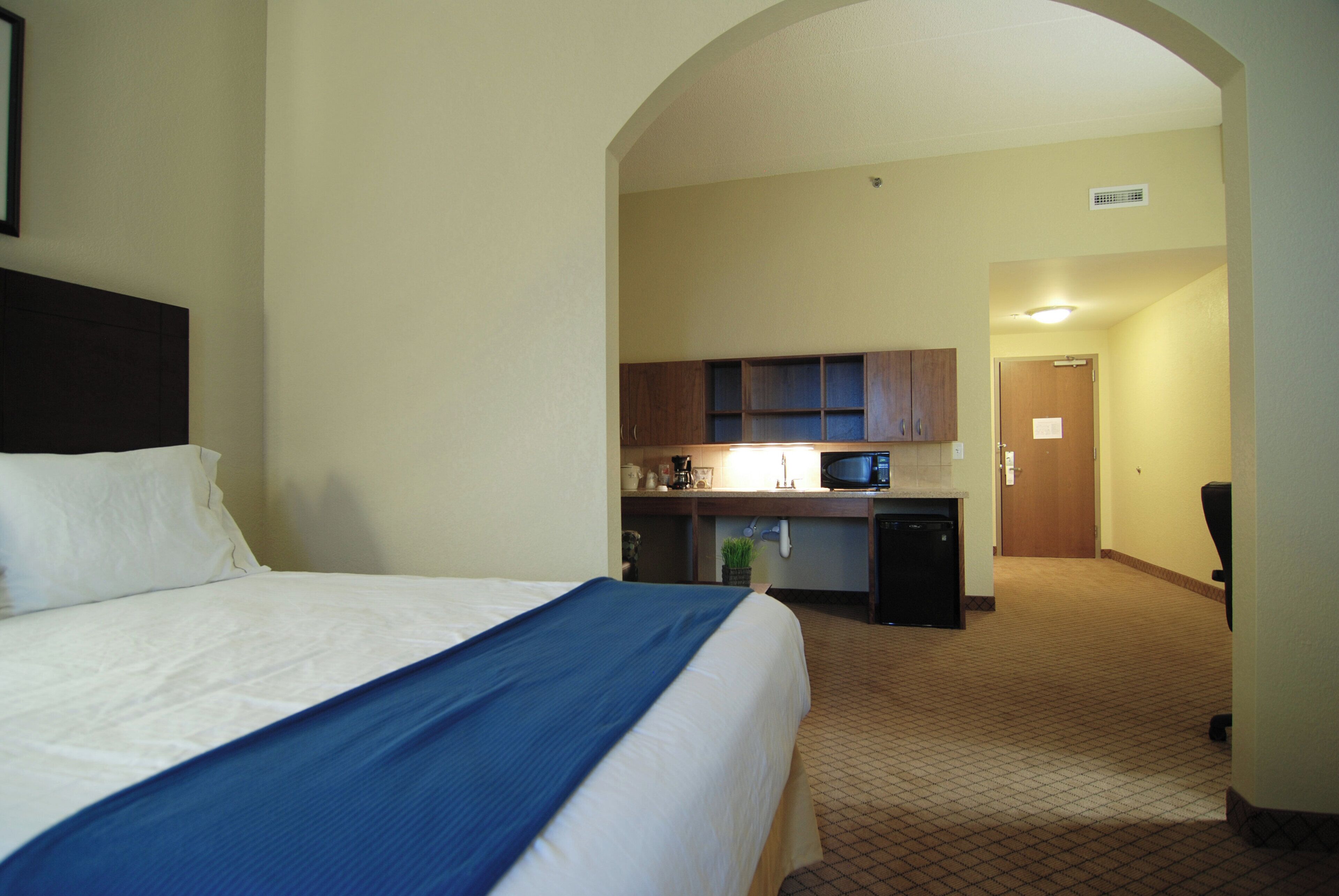 A hotel room with a bed, a kitchenette, and a bathroom.