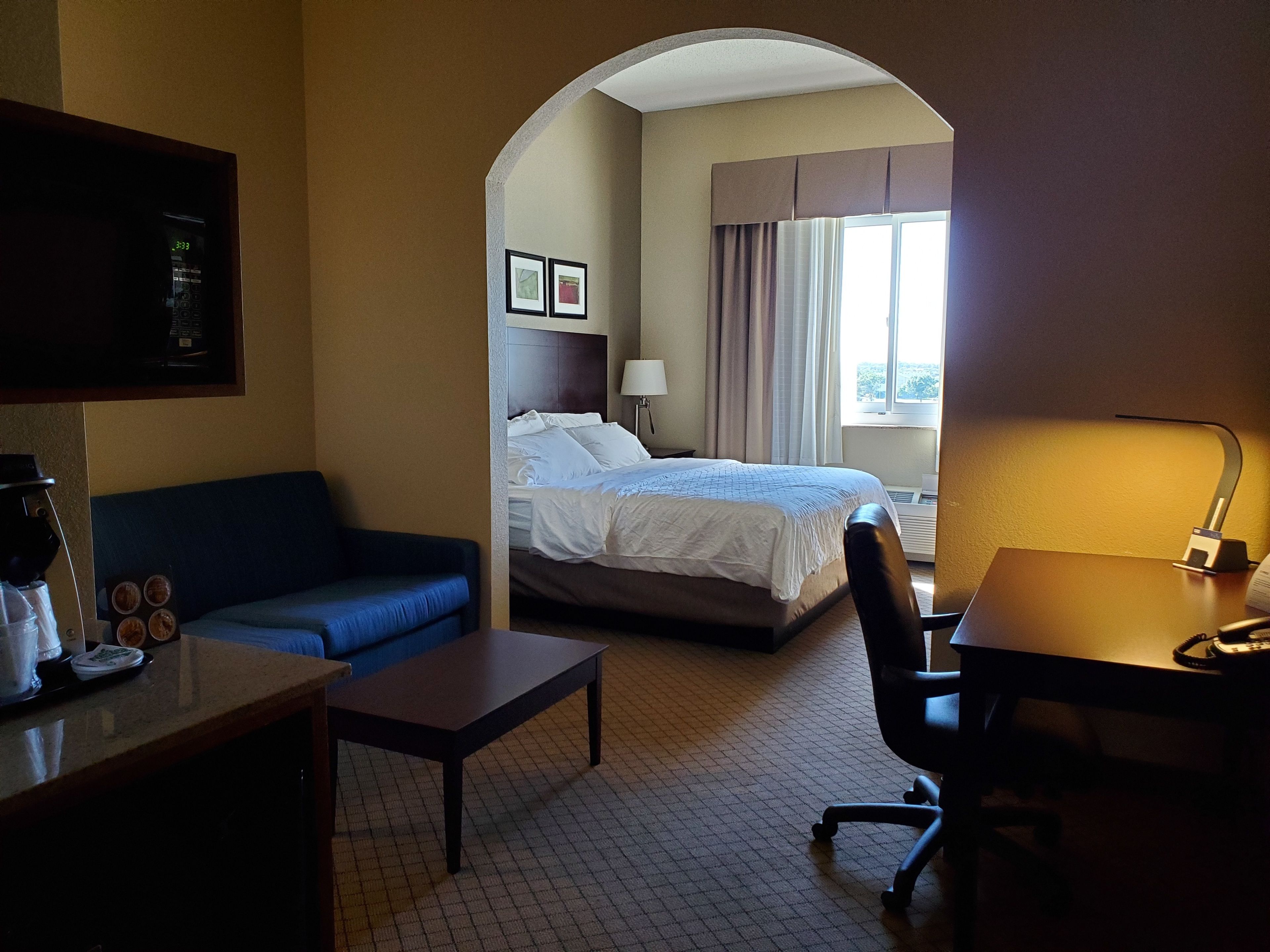 Una habitación de hotel con cama, escritorio, silla, cafetera y televisor.