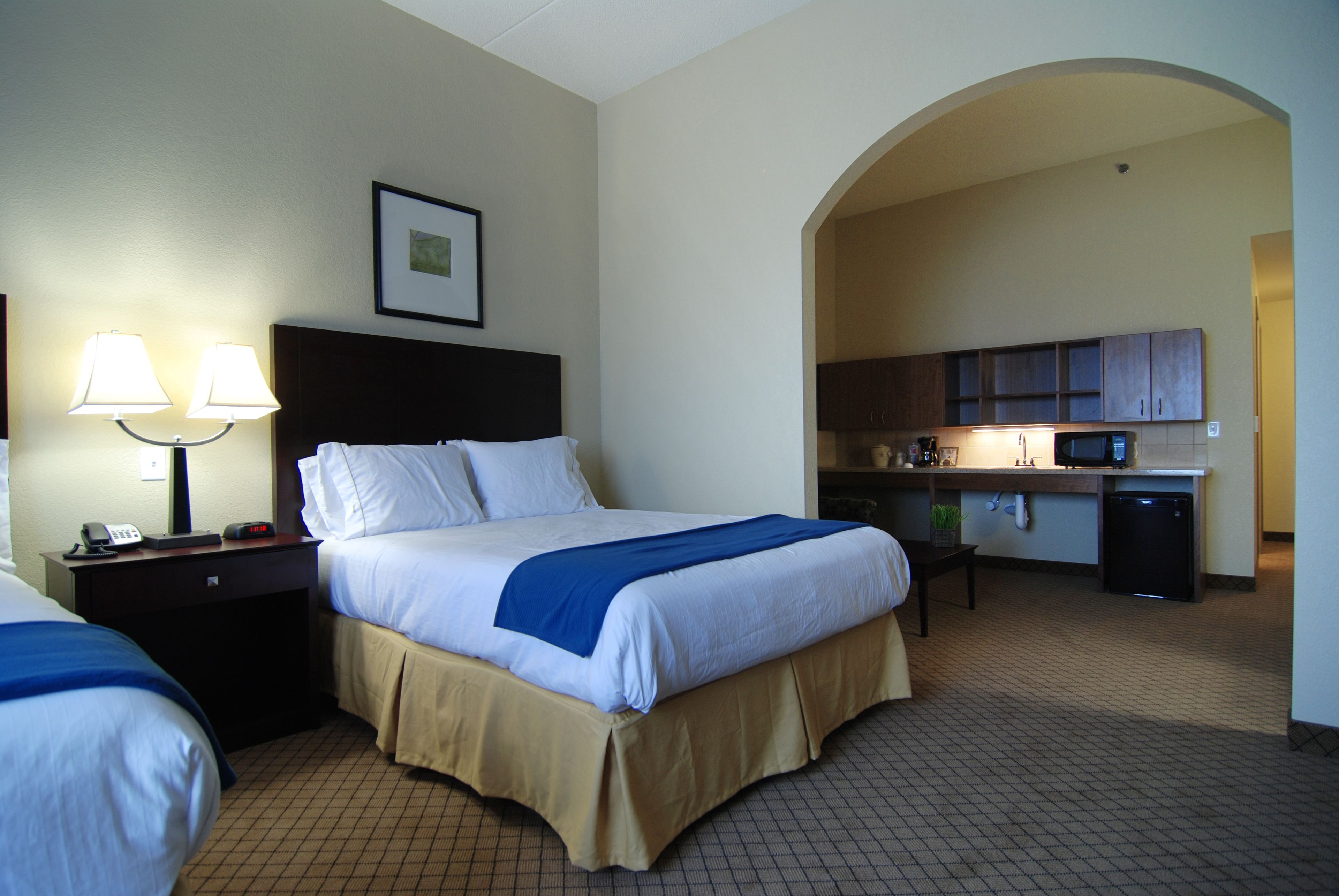 A hotel room with a bed, bedside tables, lamps, a microwave, and a kitchenette.