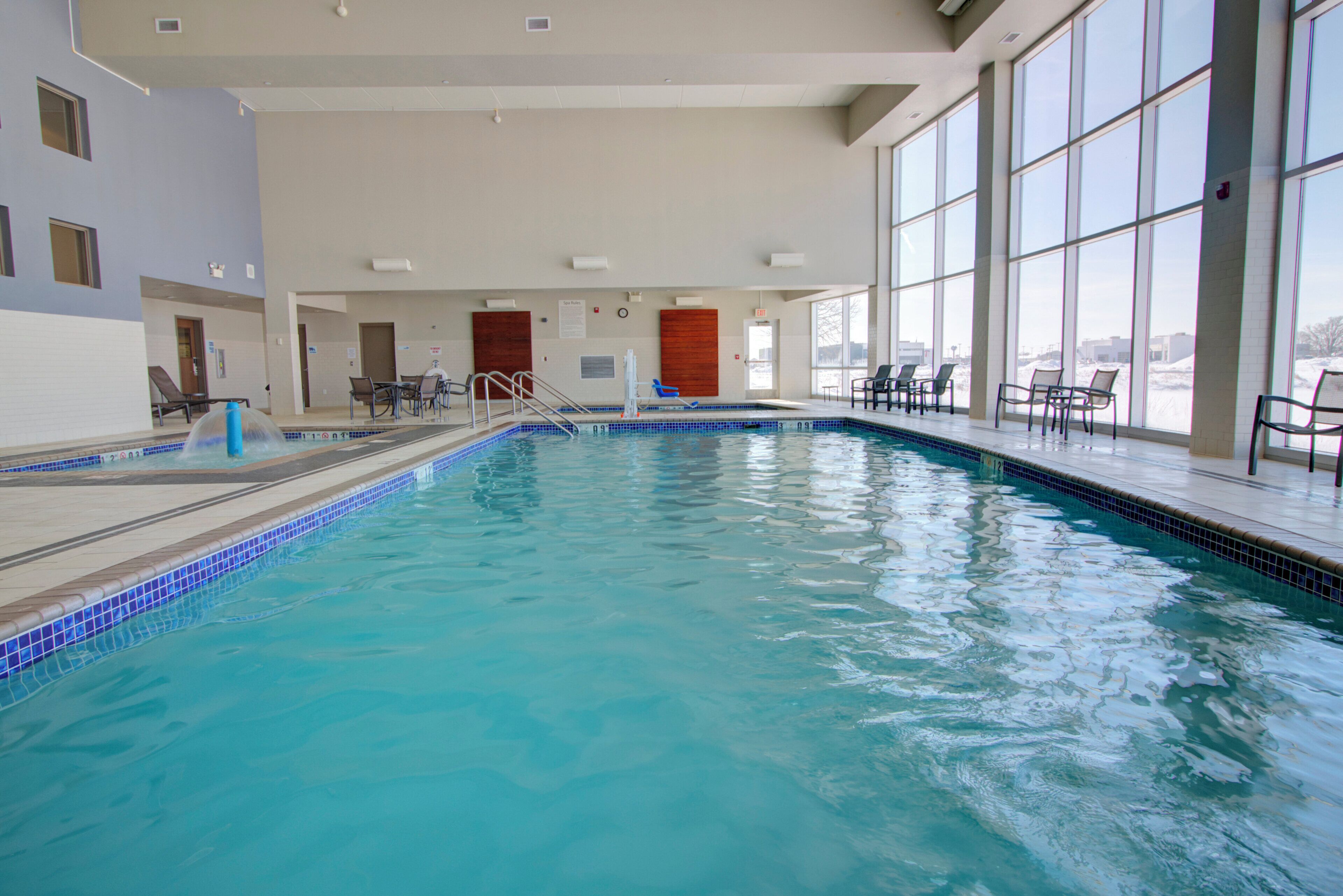 An indoor swimming pool with clear blue water, surrounded by windows and indoor seating areas.