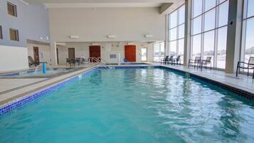 An indoor swimming pool with clear blue water, surrounded by windows and indoor seating areas.