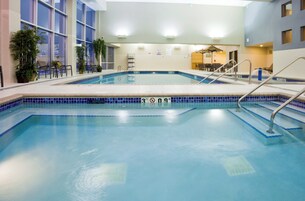 Una piscina con borde de azulejos, un puesto de salvavidas y una zona de estar con sillas y mesas.