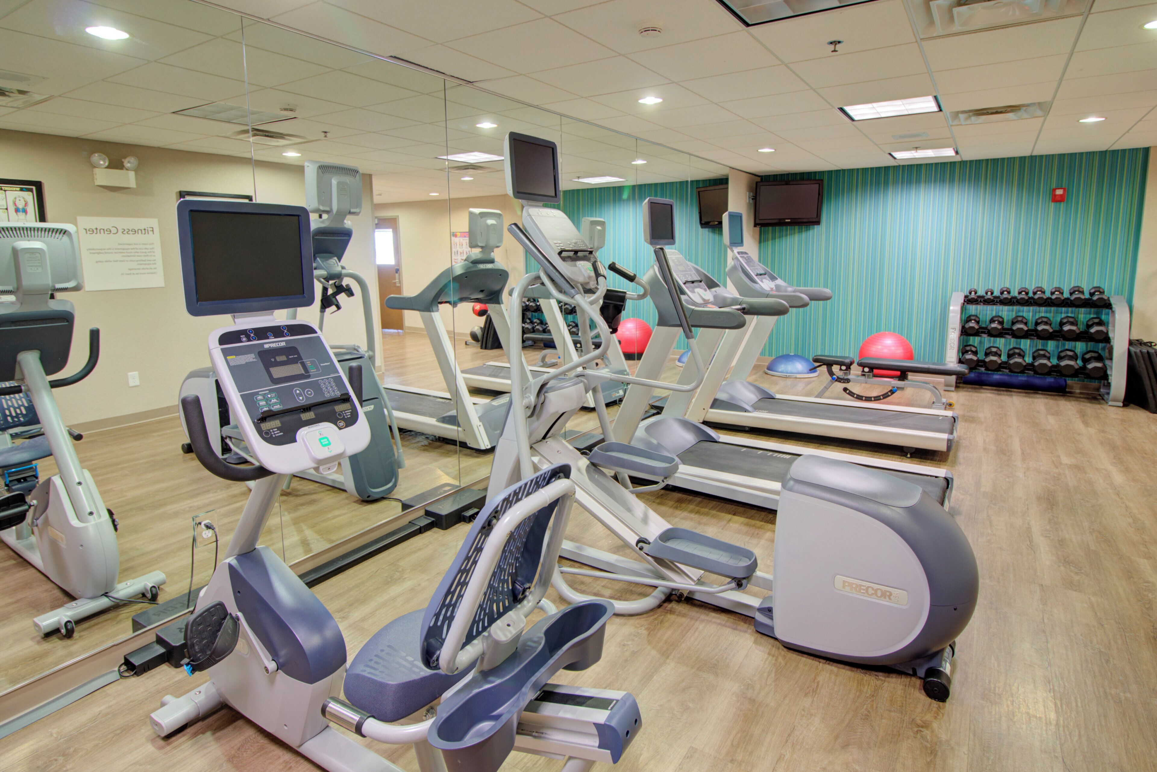 Un gimnasio con varios equipos de ejercicio, incluyendo cintas de correr, elípticas y bicicletas estáticas.