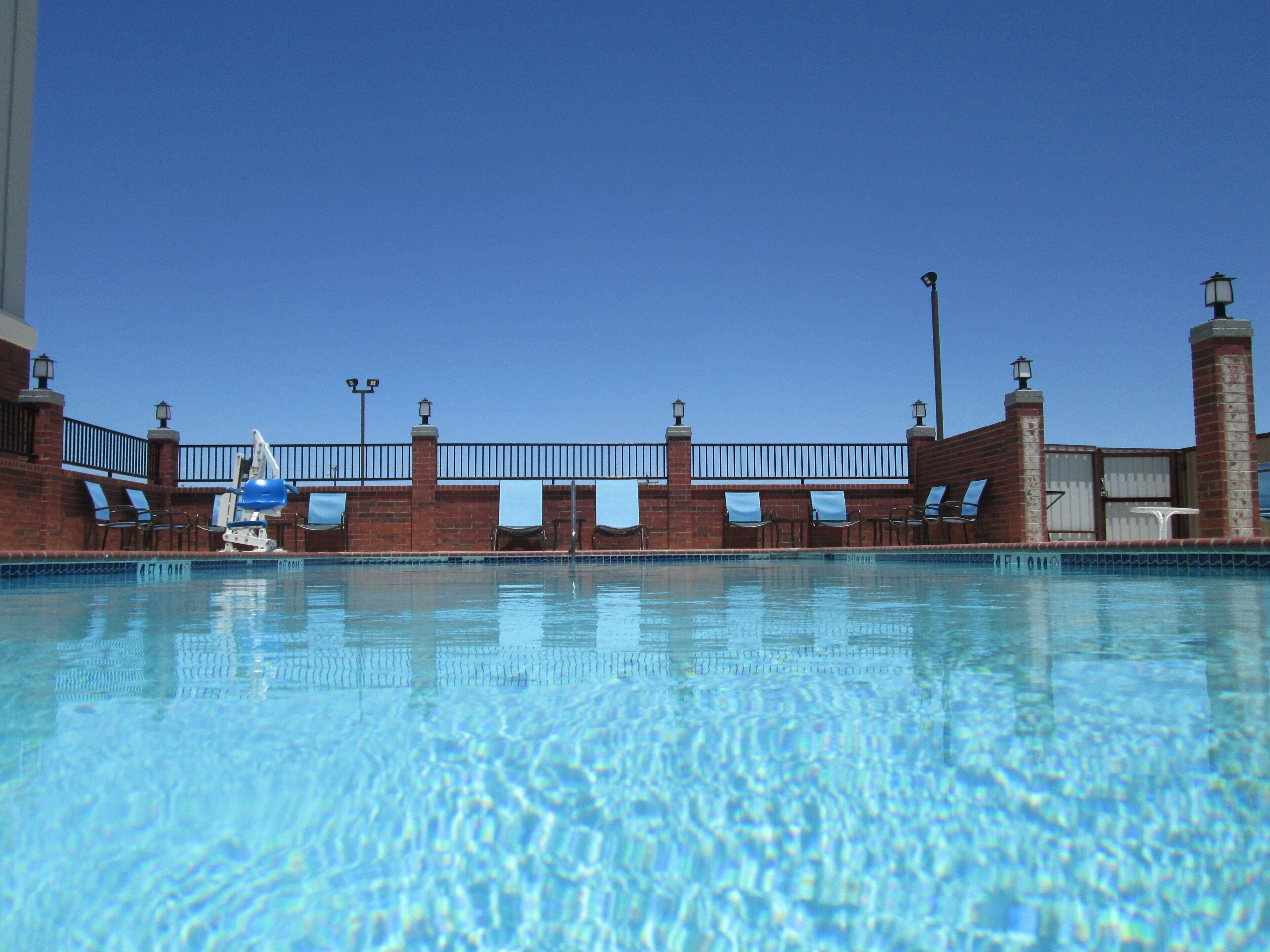 A clear blue pool with a brick wall, lounge chairs, and a lamp post.