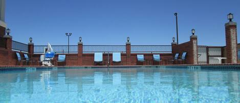 A clear blue pool with a brick wall, lounge chairs, and a lamp post.