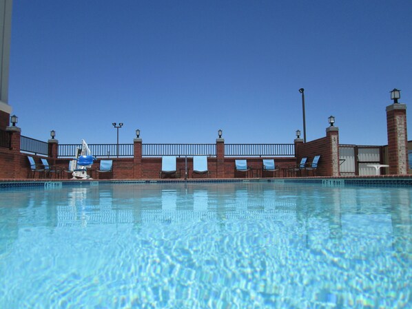 A clear blue pool with a brick wall, lounge chairs, and a lamp post.
