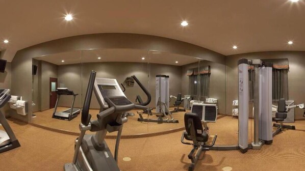 Ein Fitnessraum in einem Hotel mit Cardiogeräten, Krafttrainingsgeräten und einem Spiegel.