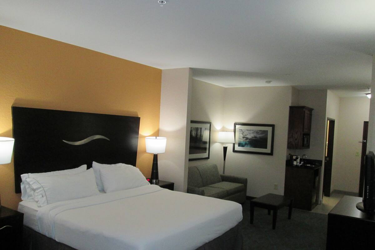 Ein Hotelzimmer mit einem großen Bett, zwei Nachttischlampen, einem Schreibtisch, einem Stuhl und einem kleinen Tisch.