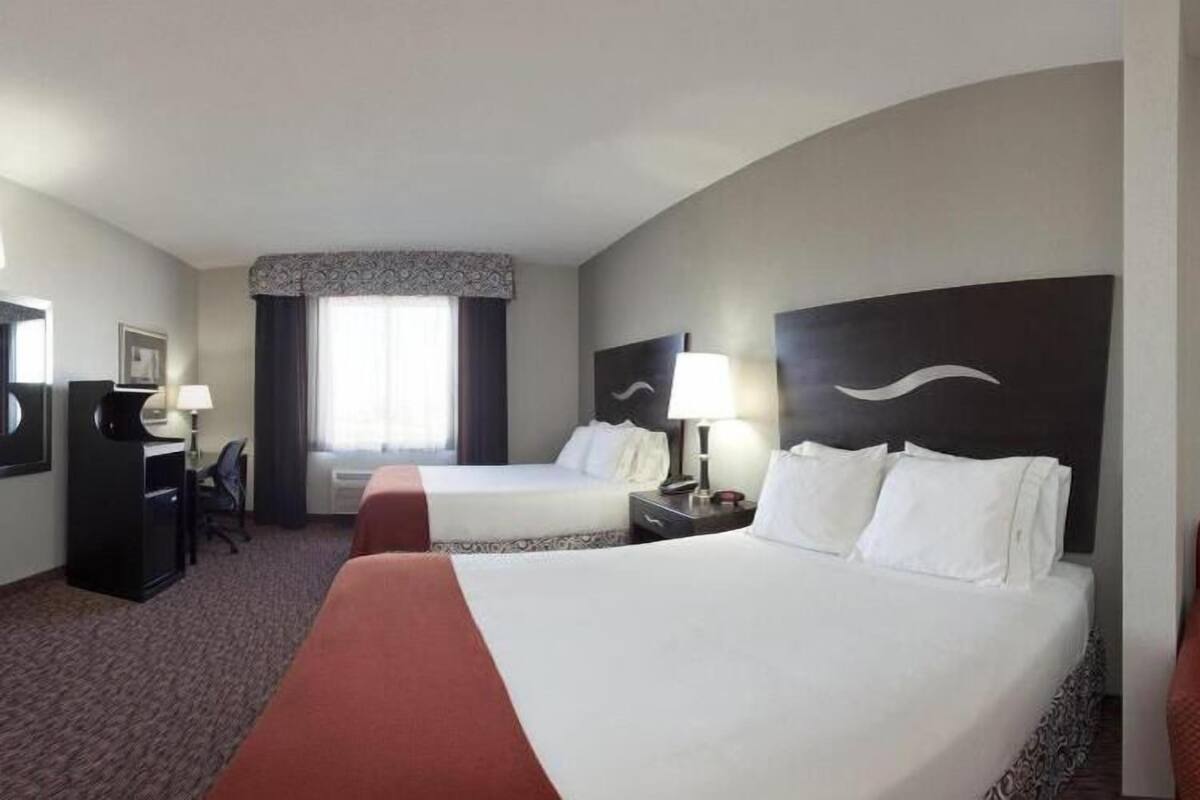 Ein Hotelzimmer mit zwei Betten, einem Schreibtisch, einem Stuhl und einem großen Fenster.