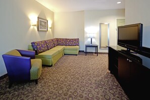 A hotel room with a sectional sofa, a flat-screen TV, a lamp, and a patterned carpet. - Holiday Inn Express & Suites Clemson by IHG (Clemson)