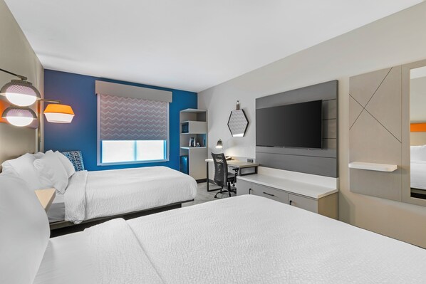 Una habitación de hotel con dos camas, un escritorio, un televisor y una ventana con cortinas decoradas.