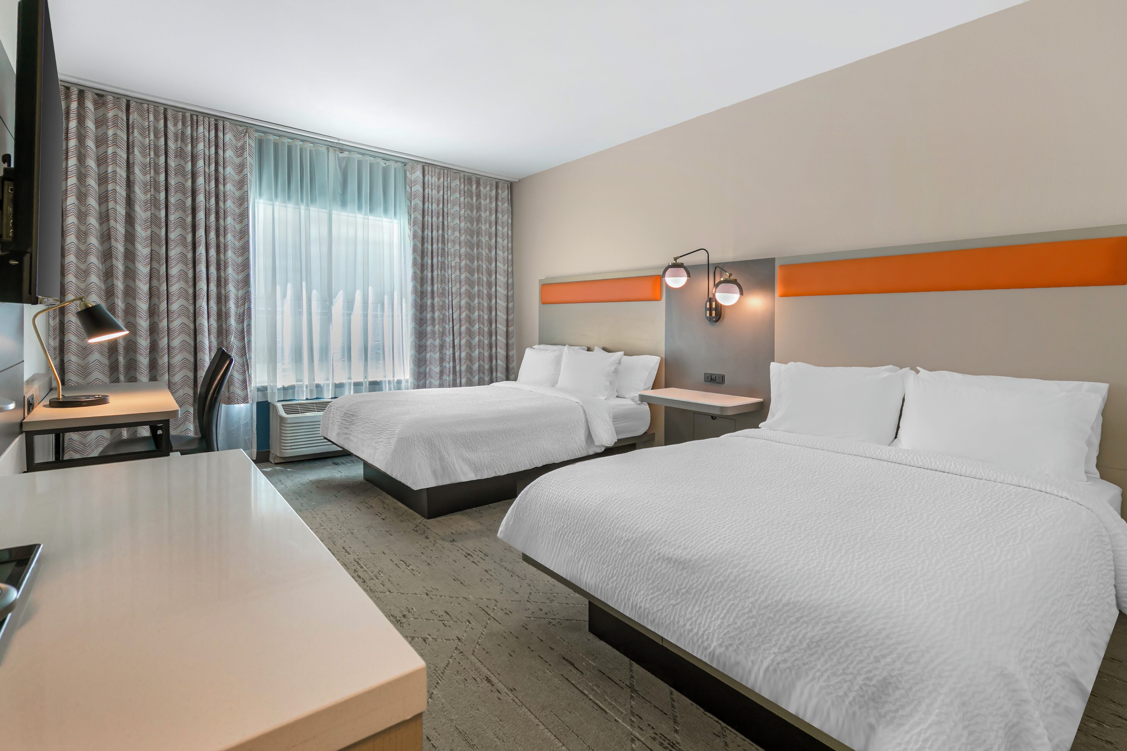 Hotellihuone, jossa on kaksi sänkyä, työpöytä, tuoli, televisio ja ikkuna, jossa on verhot.