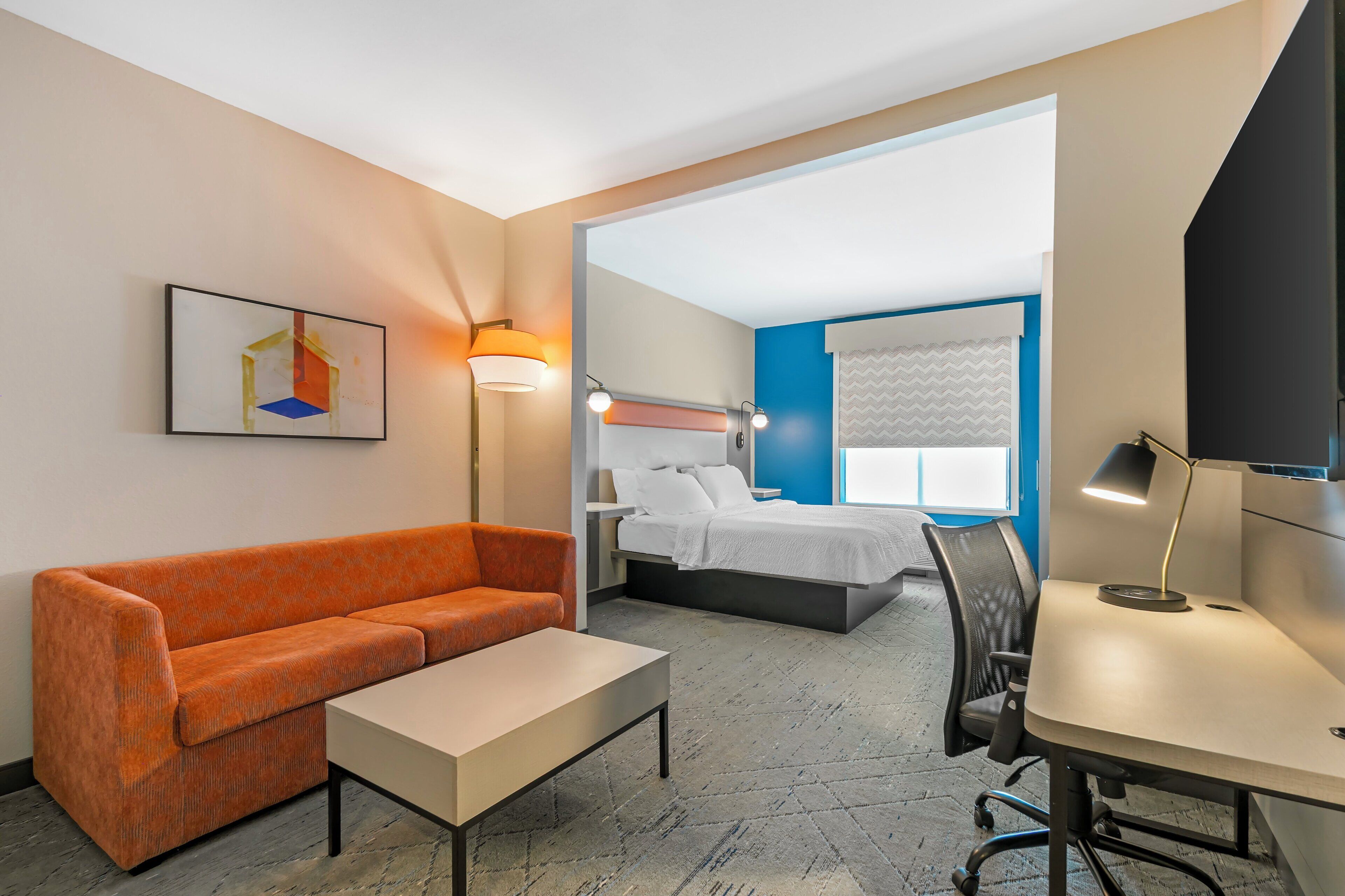 Ein Hotelzimmer mit Sofa, Schreibtisch, Bett und Fernseher.
