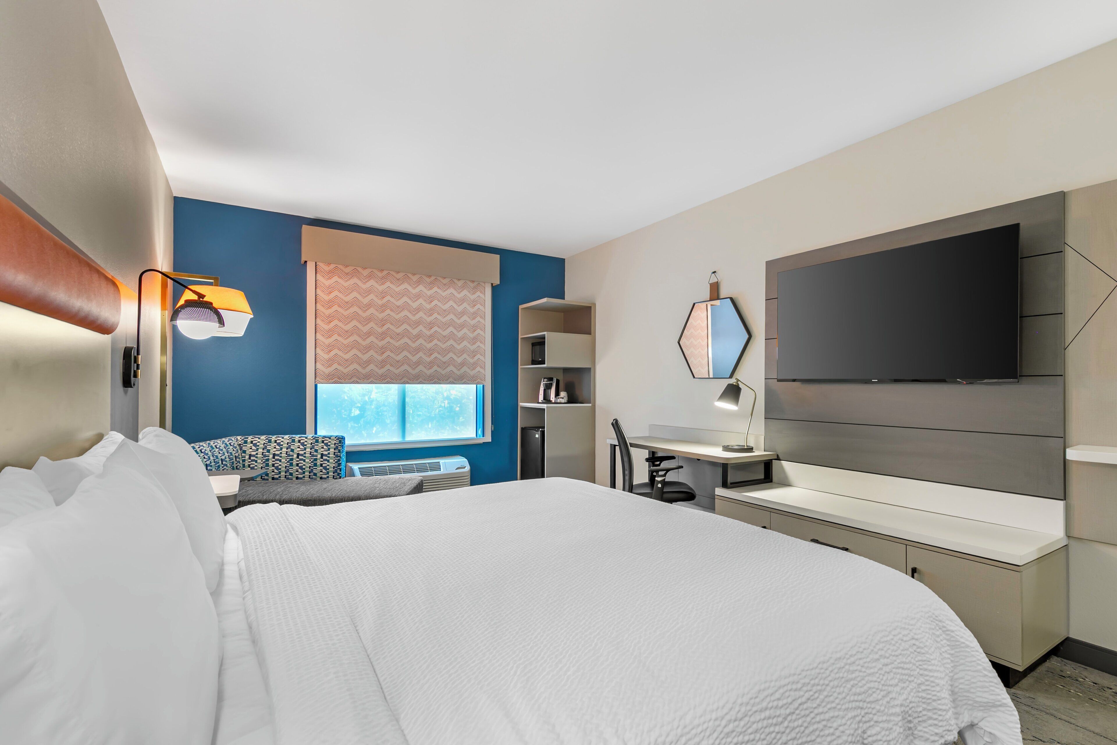 A hotel room with a bed, a desk, a television, and a window with a view.