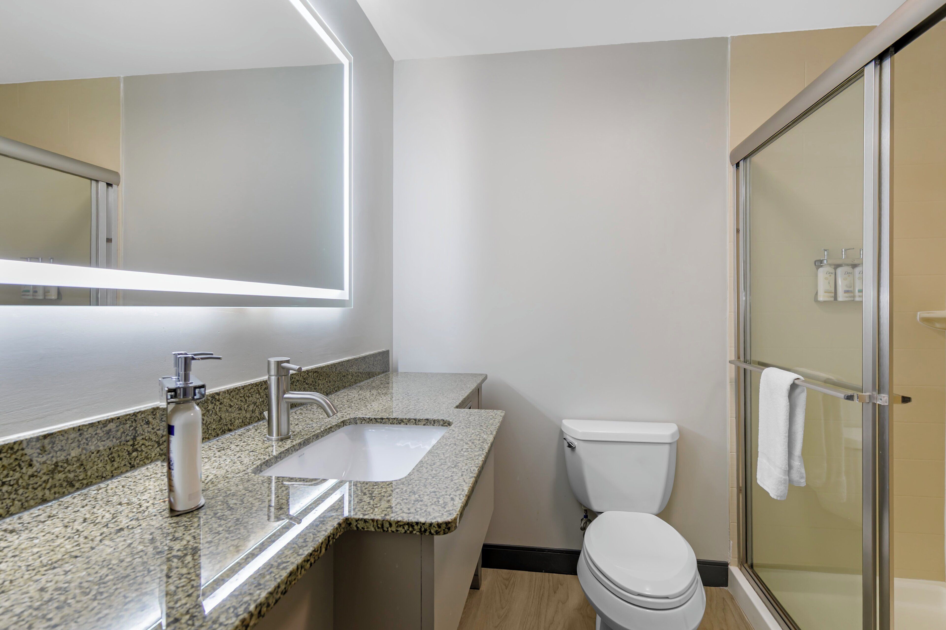 A modern bathroom with a granite countertop, a white toilet, and a glass shower enclosure.