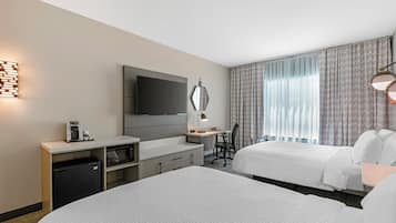 A hotel room with two beds, a desk, a flat-screen TV, a coffee machine, and a microwave.