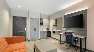 A compact living space with a sofa, a desk, a television, and a kitchenette.