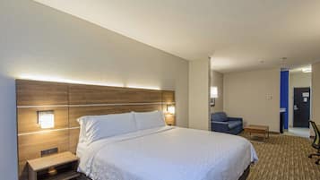 Habitación de hotel con una cama grande, lámparas de noche, una mesita de noche, una pequeña mesa, una silla azul y una puerta que da a un baño.