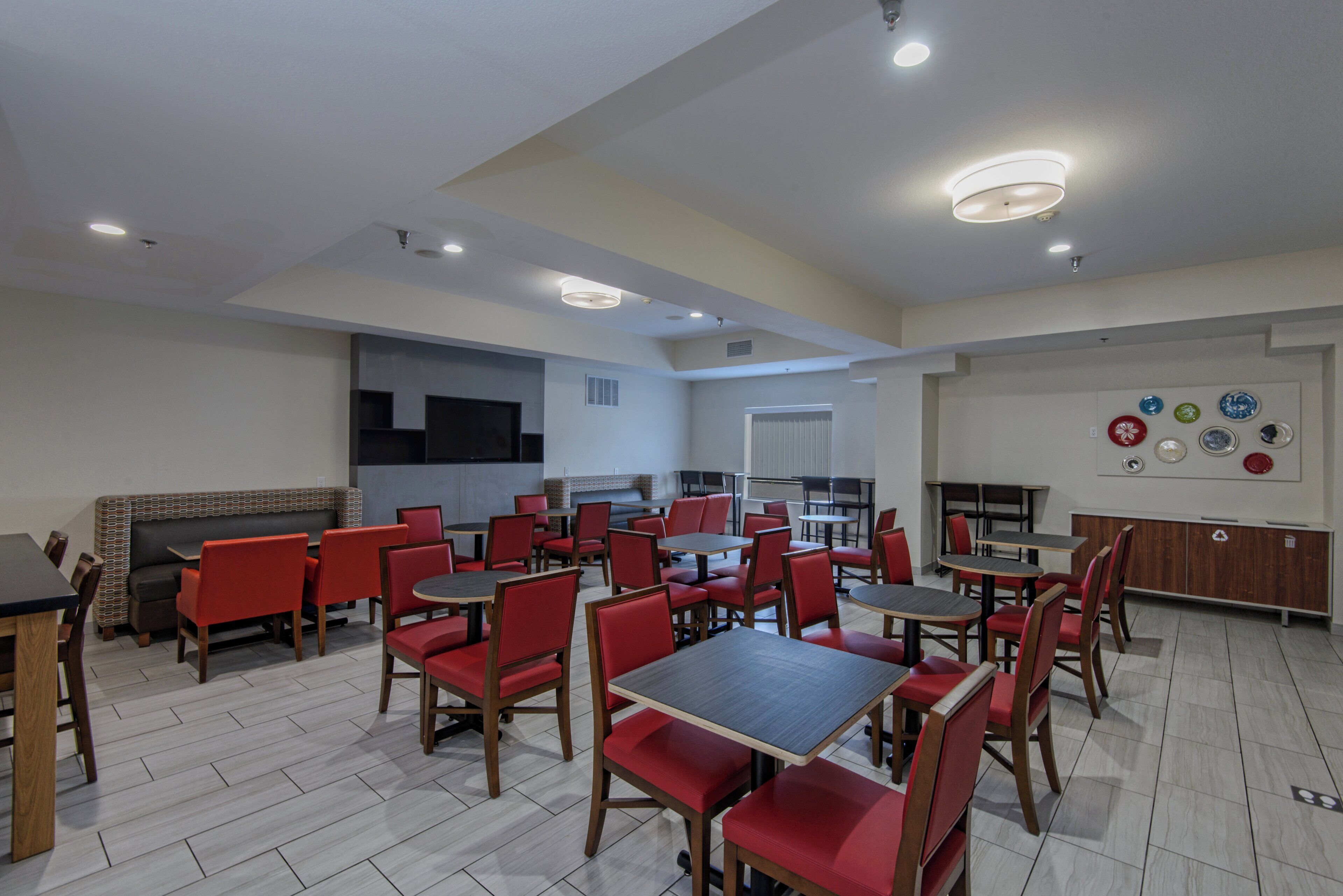 A modern dining area with multiple tables and chairs, a kitchen area, and a wall with decorative plates.