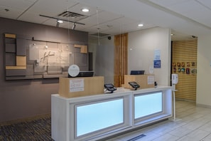 A hotel reception desk with a digital check-in kiosk, a wooden panel wall, and a sign thanking guests for social distancing. - Holiday Inn Express Hotel & Suites Corpus Christi by IHG (Corpus Christi)