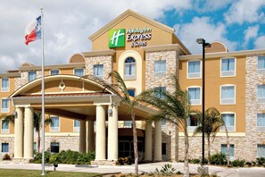 A Holiday Inn Express hotel with a stone facade, a covered entrance, and palm trees. - Holiday Inn Express Hotel & Suites Corpus Christi by IHG (Corpus Christi)