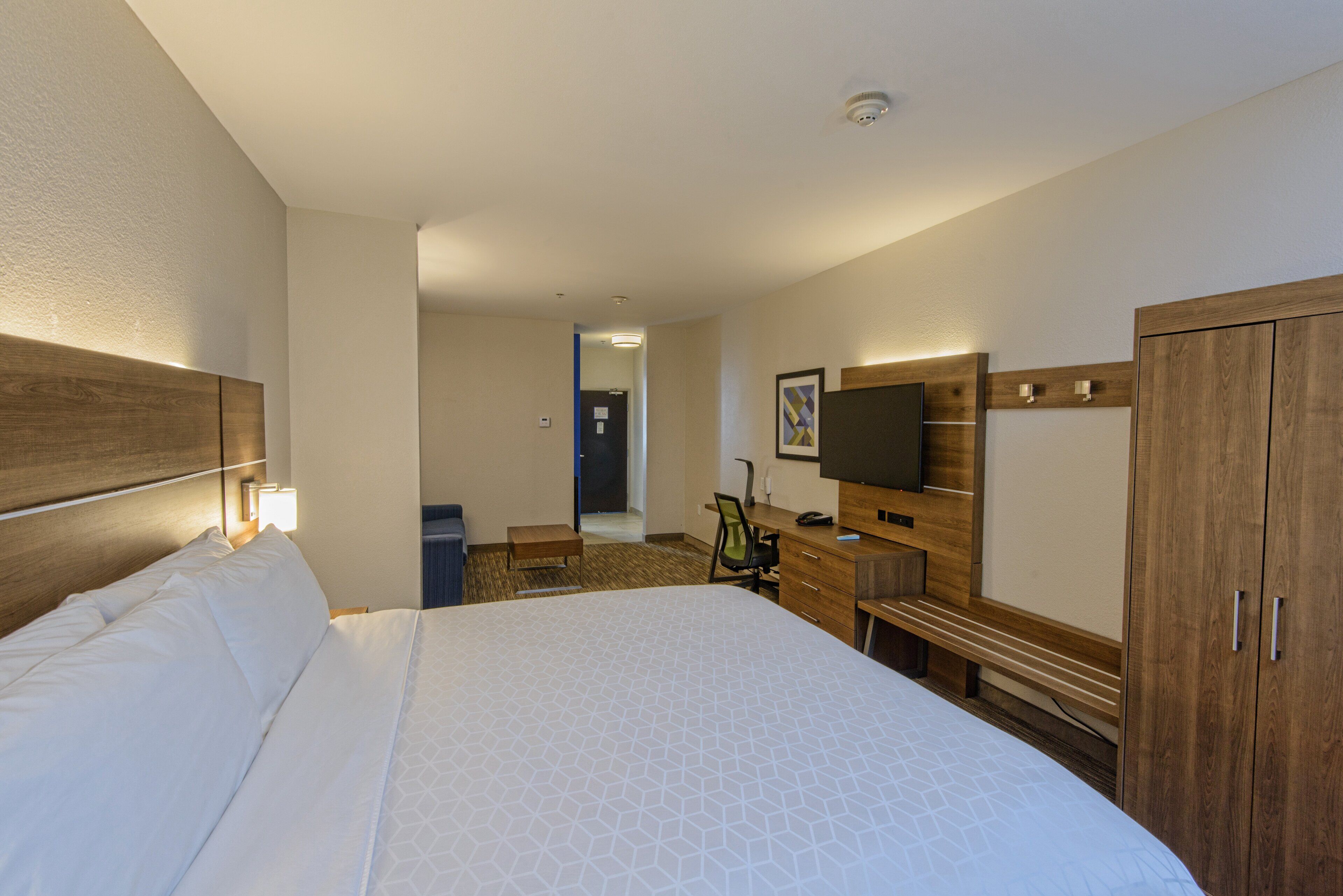 Une chambre d’hôtel avec un grand lit, un bureau avec une chaise, une télévision et une armoire.