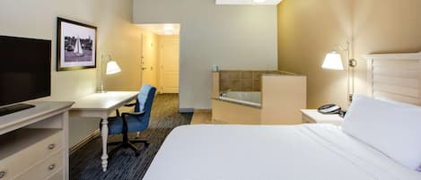 Habitación de hotel con cama, escritorio, silla, televisión y baño con bañera e inodoro.