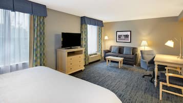 A hotel room with a large bed, a TV, a sofa, a desk, and a lamp.