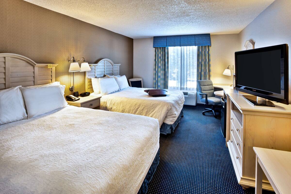 Une chambre d’hôtel avec deux lits, un bureau, un téléviseur à écran plat, une chaise et une commode.